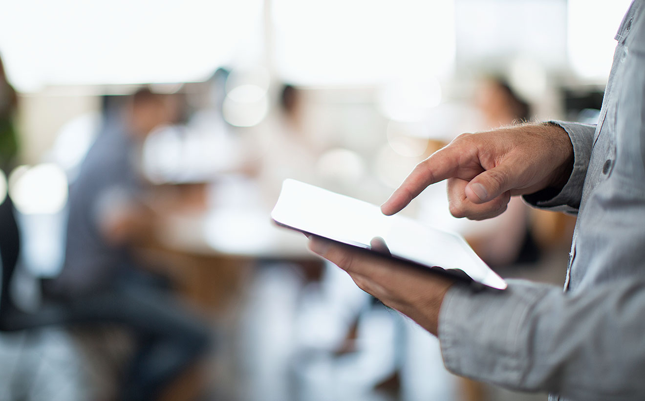 Ein Mann im Hemd hält ein Tablet und tippt darauf