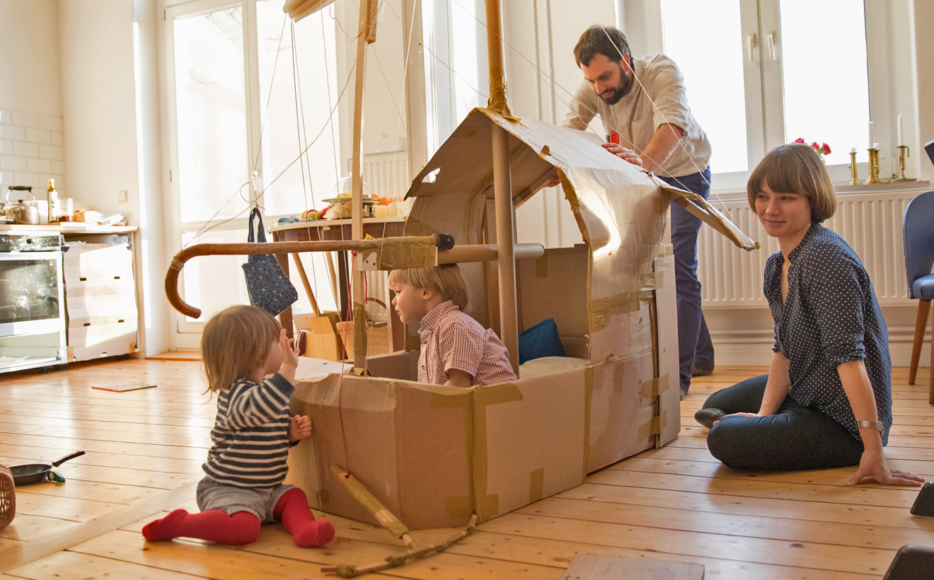Kleine Kinder spielen mit ihren Eltern in einem Pappschiff, das in der Küche steht