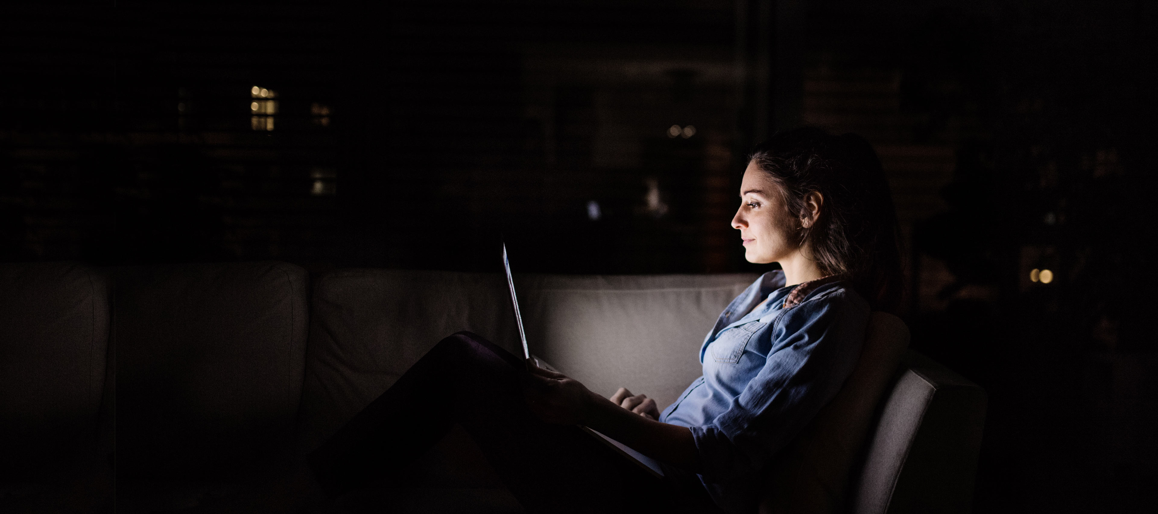 Frau sitzt im Dunkeln vor ihrem Laptop.