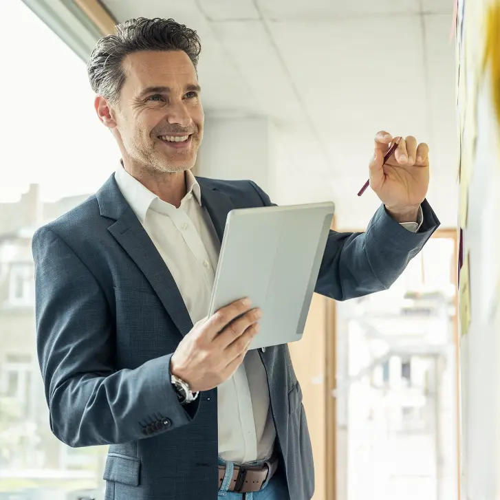 Mann in Businesskleidung hält Tablet und schreibt etwas auf ein Whiteboard
