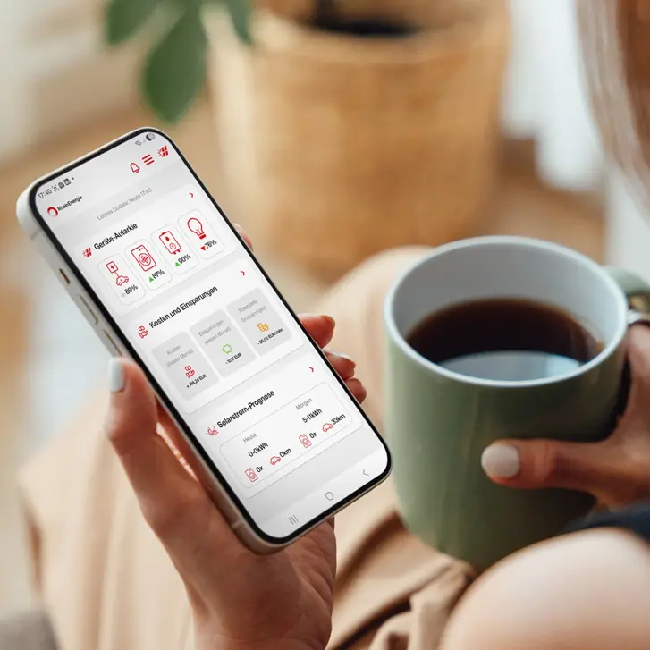 Hand hält Handy mit App zum Home Energy Management System und Kaffeetasse