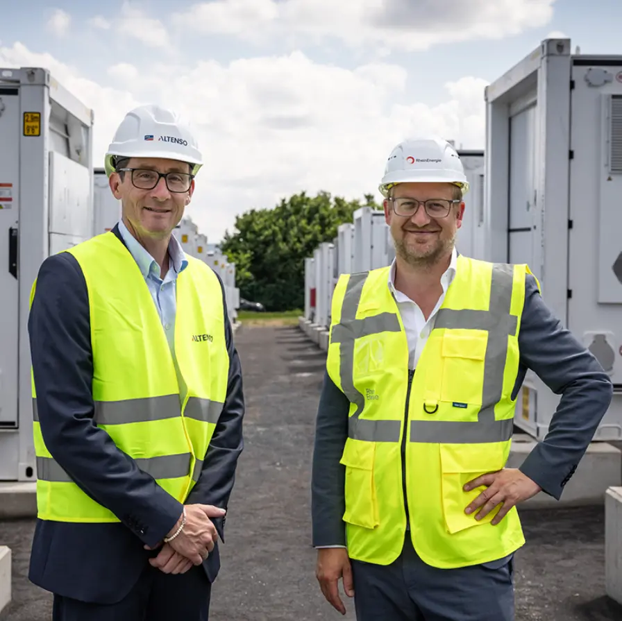 Zwei Männer mit gelben Warnwesten stehen vor einem großen Batteriespeicher.