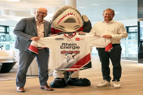 Philipp Walter (KEC) und Stephan Segbers (RheinEnergie) halten ein Haie-Trikot in die Kamera.