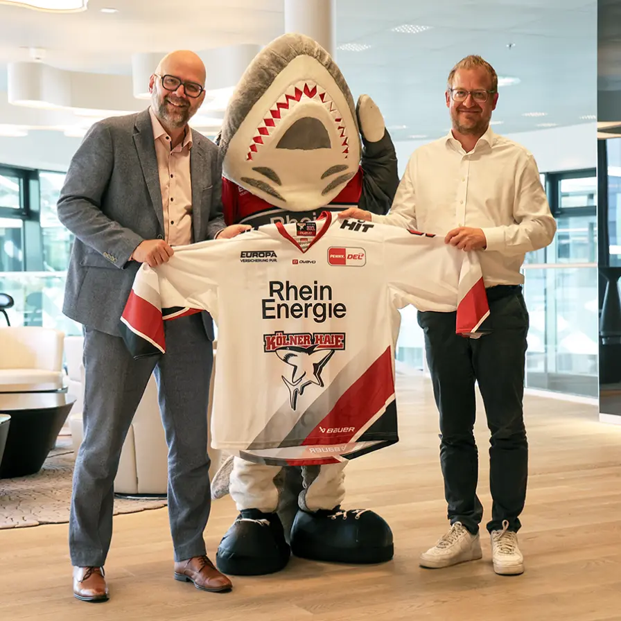 Philipp Walter (KEC) und Stephan Segbers (RheinEnergie) halten ein Haie-Trikot in die Kamera.
