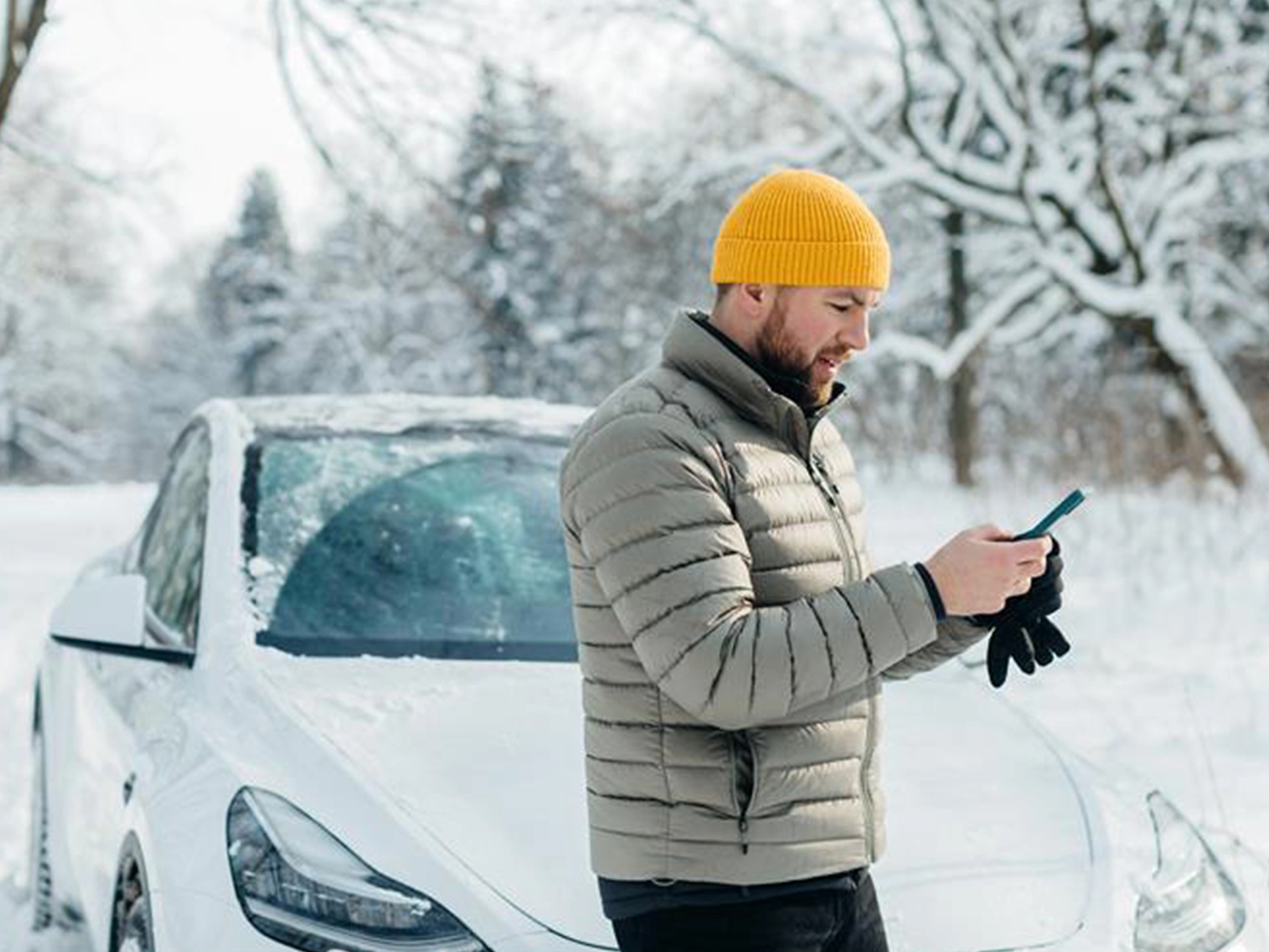 Ein Mann steht im Schnee vor seinem Auto und schaut auf sein Handy
