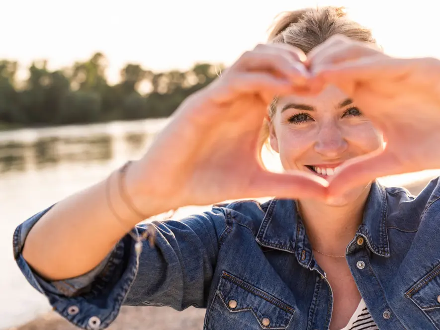 Junge Frau bildet Herz mit ihren Händen.