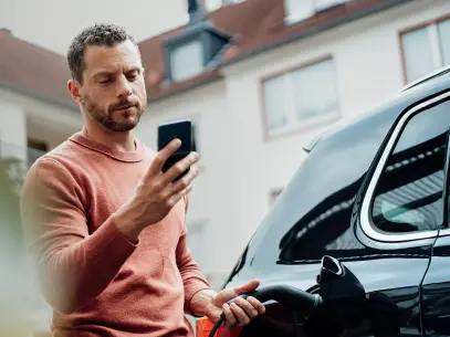 Ein Mann lädt sein schwarzes Elektroauto und schaut dabei auf sein Handy.