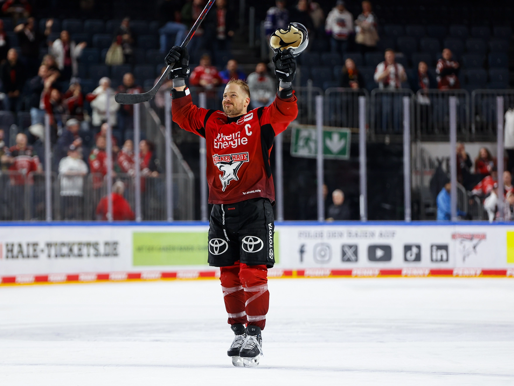 Ein man steht in Hockey Ausrüstung mit erhobenen Armen auf dem Eis im Stadion