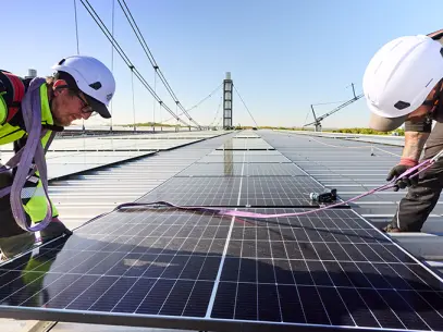 Zwei Techniker installieren ein Photovoltaik-Modul auf dem Dach des RheinenergieSTADION. 