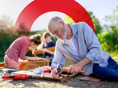 Älterer Mann nagelt Holzlatte mit einem Hammer fest.
