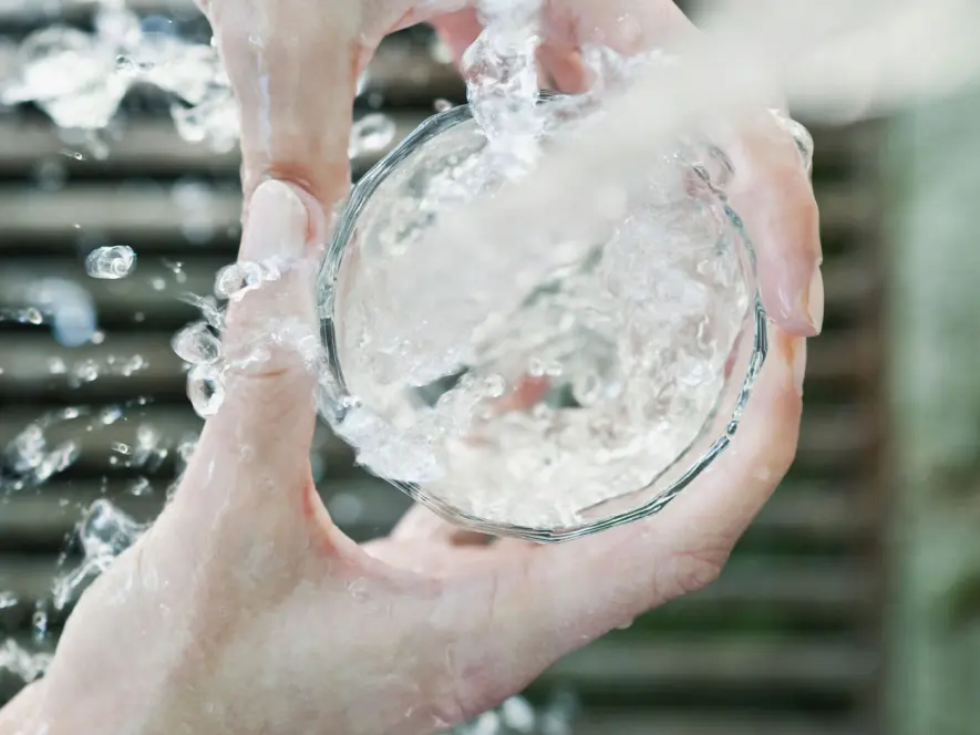 Wasserglas unter einem Trinkbrunnen.