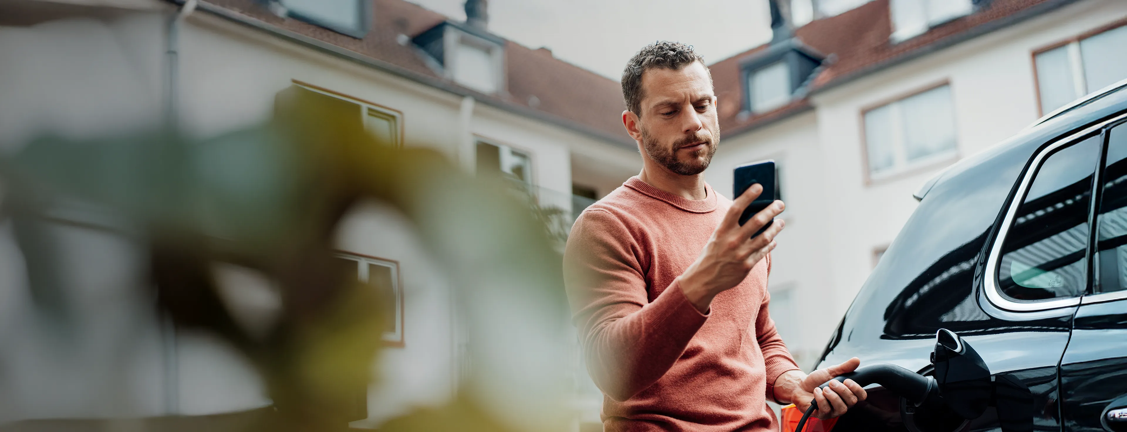 Mann lädt sein E-Auto und schaut auf sein Handy.