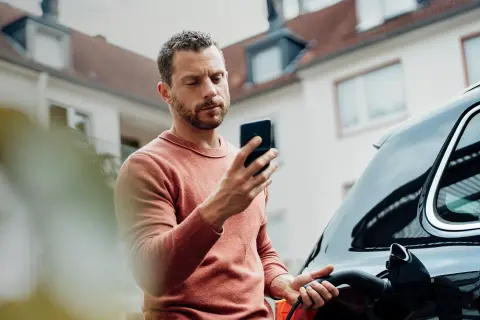 Mann lädt sein E-Auto und schaut auf sein Handy.