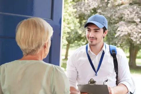 Eine ältere Dame öffnet einem jungen Mann die Tür