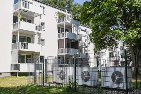 Eingezäunte Wärmepumpen vor einem Mehrfamilienhaus.