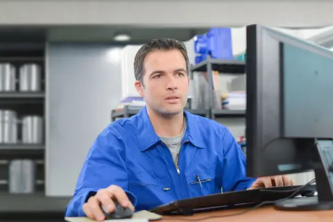 Ein Mensch im Blaumann sitzt vor einem Computerbildschirm