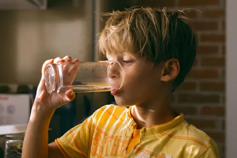 Ein Junge trinkt Wasser aus einem Glas.