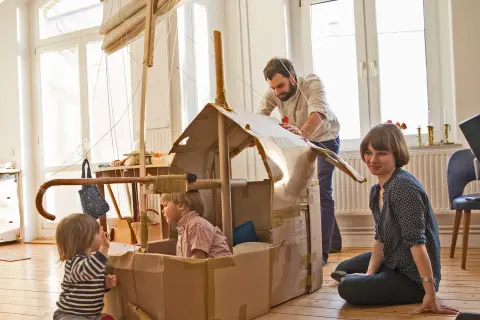 Kleine Kinder spielen mit den Eltern in einem Pappschiff in der Küche
