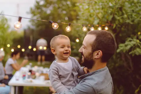 Vater mit Kind auf dem Arm bei einer Gartenparty.