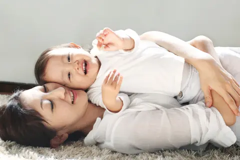 Kind liegt mit der Mutter auf dem Fußboden.