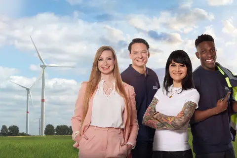 Zwei Frauen und zwei Männer stehen vor Windrädern auf einer grünen Wiese
