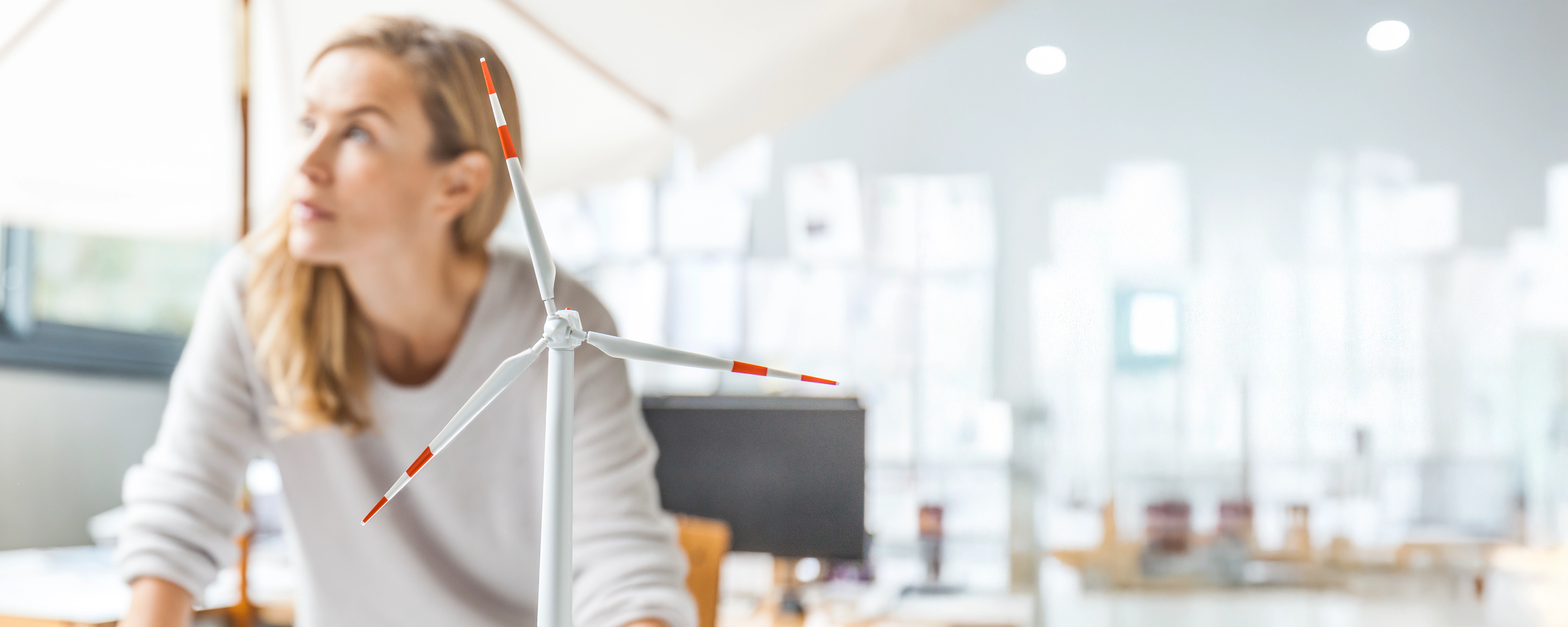 Frau steht am Schreibtisch neben ihr ein Windradmodel