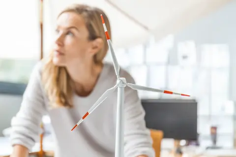 Frau steht am Schreibtisch neben ihr ein Windradmodel