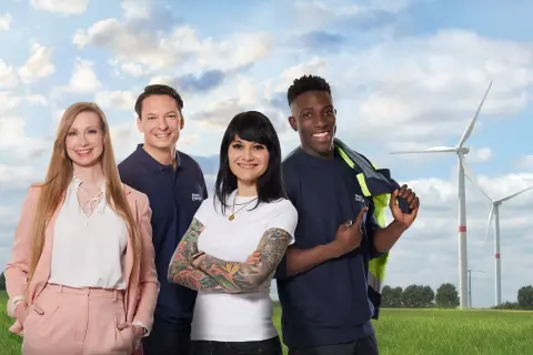 Zwei Frauen und zwei Männer stehen vor Windrädern auf einer grünen Wiese