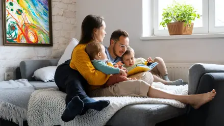 Elternpaar und zwei kleine Kinder sitzen auf dem Sofa und lesen.