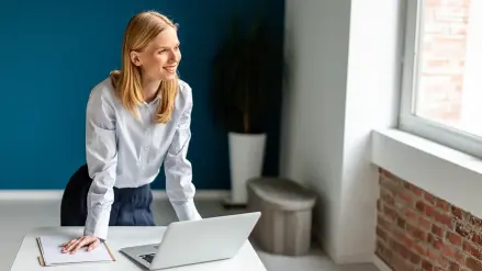 Frau stützt sich auf Schreibtisch vor Laptop ab