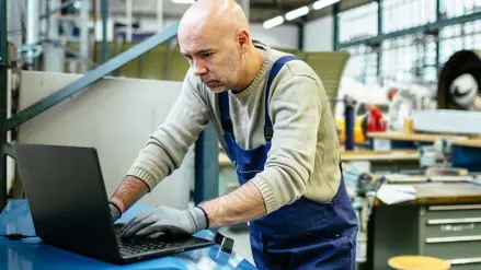Ein Handwerker im Blaumann steht am Laptop