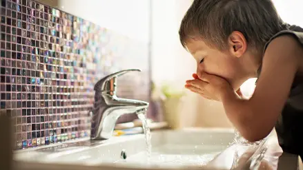 Junge im Badezimmer trink Wasser aus dem Hahn.