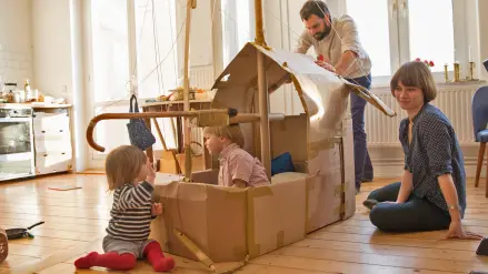 Kleine Kinder spielen mit ihren Eltern in einem Pappschiff, das in der Küche steht
