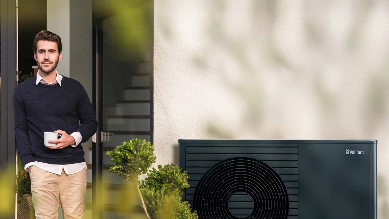 Mann, Frau und drei Kinder laufen Hand in Hand auf einer Wiese vor einem Haus mit Wärmepumpe