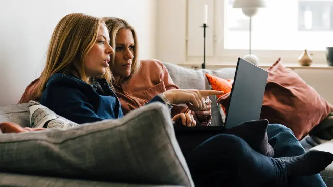 Zwei Frauen sitzen auf dem Sofa mit einem Laptop.
