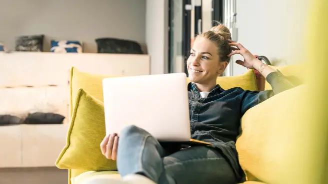Frau sitzt auf einem gelben Sofa mit Laptop.