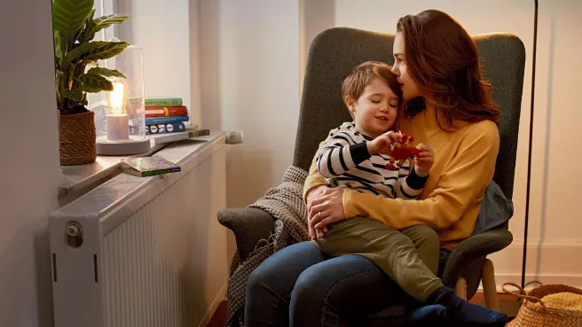 Frau und Kind sitzen vor der Heizung auf dem Sessel.