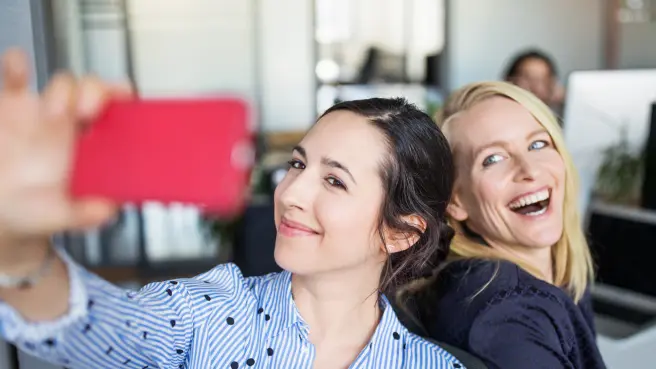 Zwei Frauen mit guter Laune im Büro machen ein Selfie von sich.