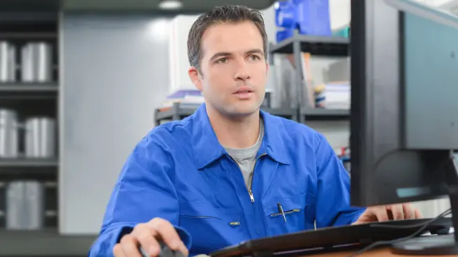 Ein Mensch im Blaumann sitzt vor einem Computerbildschirm