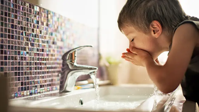 Junge im Badezimmer trink Wasser aus dem Hahn.