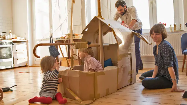 Kleine Kinder spielen mit ihren Eltern in einem Pappschiff, das in der Küche steht