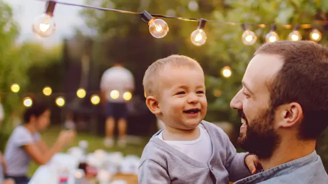 Mann mit Kind auf dem Arm bei einer Gartenparty.