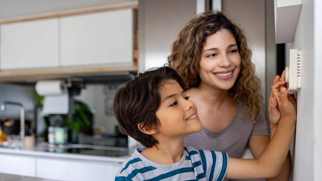 Mutter und Sohn schauen auf das Heizthermostat was in der Küche hängt