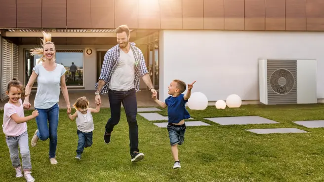 Familie im Garten vor einem Haus mit Wärmepumpe 