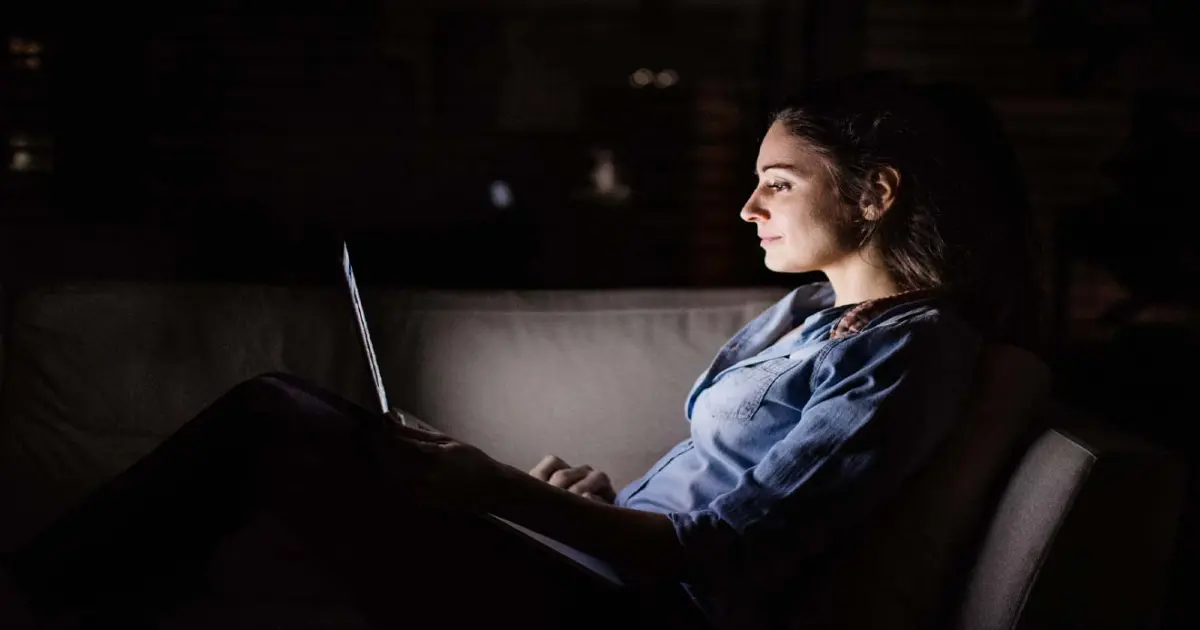 Frau sitzt im Dunkeln vor ihrem Laptop.