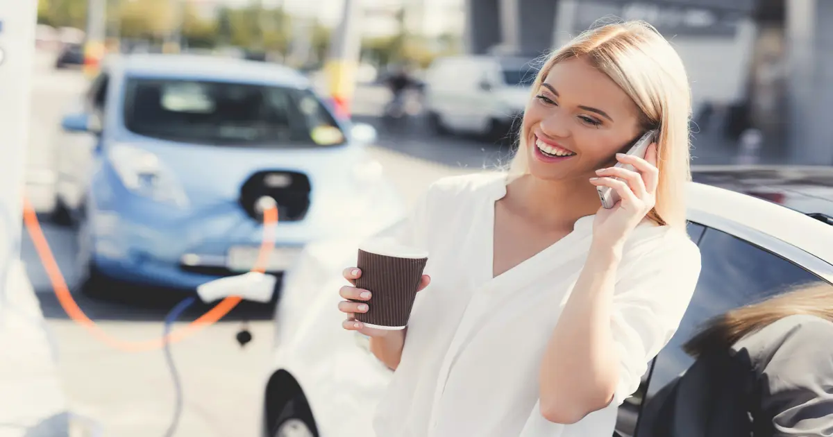 Frau lädt ihr E-Auto an einer Ladestation und telefoniert währenddessen