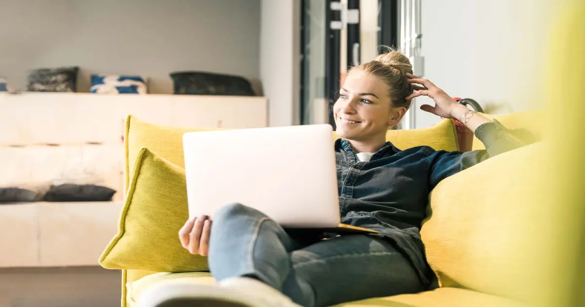 Frau sitzt auf einem gelben Sofa mit Laptop.