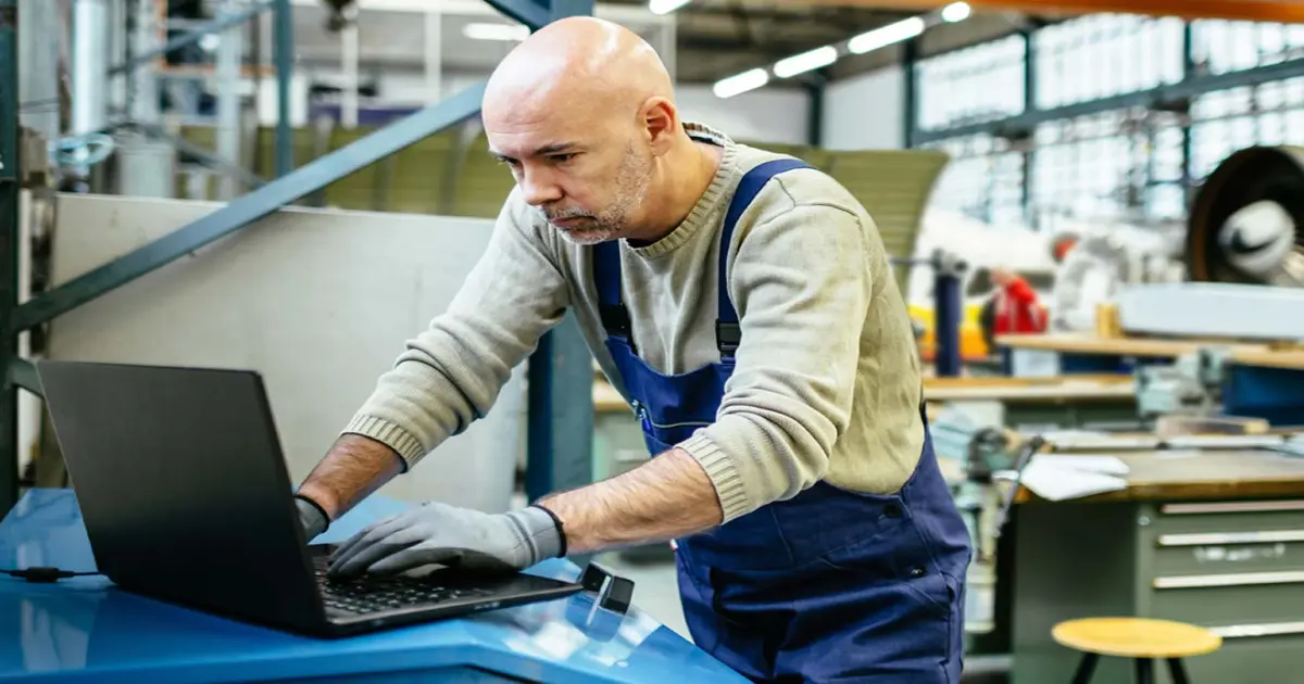 Ein Handwerker im Blaumann steht am Laptop