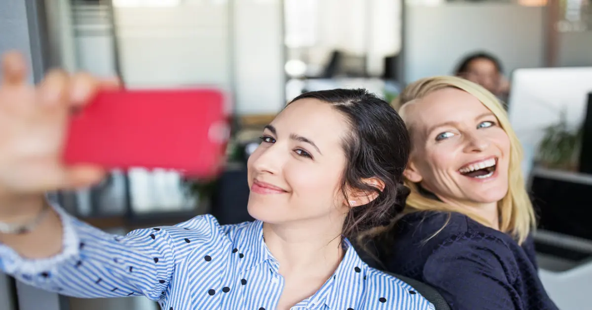 Zwei Frauen mit guter Laune im Büro machen ein Selfie von sich.