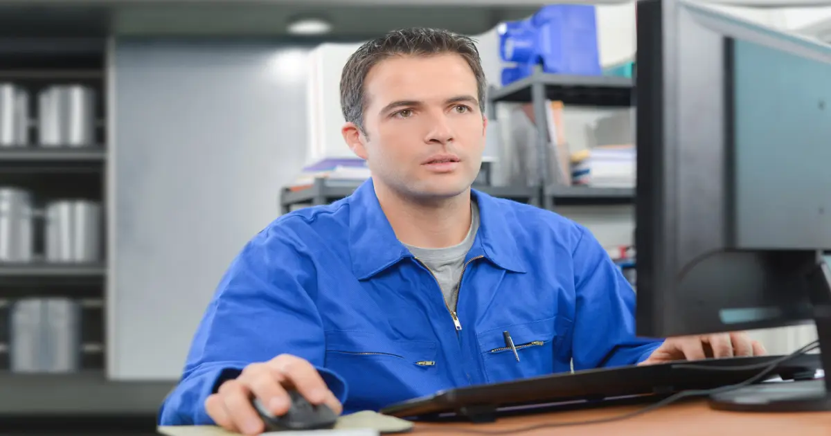 Ein Mensch im Blaumann sitzt vor einem Computerbildschirm